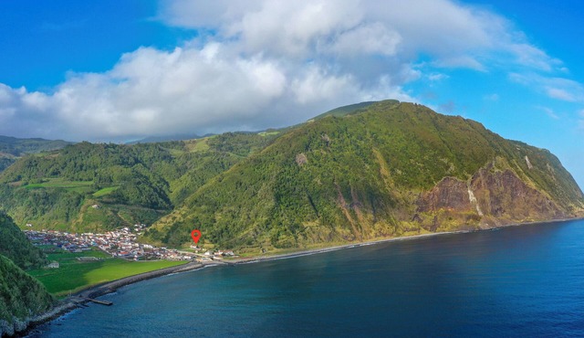 A cozy house in an imposing landscape between green hills and the blue sea.